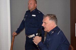 Policjanci podczas spotkania z uczniami w auli Komendy Wojewódzkiej Policji w Rzeszowie. Na pierwszym planie policjant z mikrofonem. W tle drugi policjant.