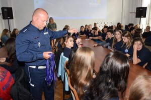 Policjanci podczas spotkania z uczniami w auli Komendy Wojewódzkiej Policji w Rzeszowie. Na pierwszym planie policjant rozdaje uczniom niebieskie smycze.