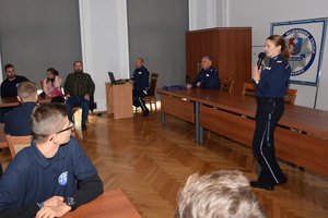 Policjanci podczas spotkania z uczniami w auli Komendy Wojewódzkiej Policji w Rzeszowie. Na pierwszym planie policjantka z mikrofonem.