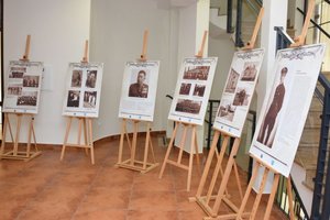 Fotografia kolorowa na której znajduje się pomieszczenie korytarza z filarami. Po prawej stronie zdjęcia widoczne jest 6 sztalug na których umieszczone są tablice  przedstawiające archiwalne fotografie funkcjonariuszy Policji Państwowej.