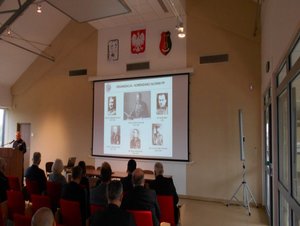 Na zdjęciu Komendant Powiatowy Policji w Stalowej Woli podczas przemówienia, w tle na ekranie slajd przedstawiający Komendantów Głównych PP
