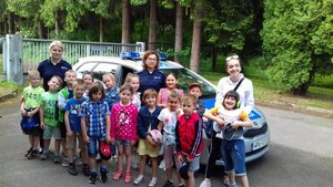 Na zdjęciu grupa dzieci wraz z policjantkami oraz opiekunem na tle policyjnego radiowozu.