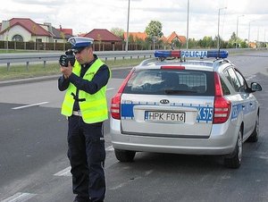 na zdjęciu policjant dokonujący pomiaru prędkości, w tle radiowóz