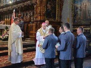Fotografia kolorowa. Bazylika ojców bernardynów w Leżajsku. Biskup w asyście współcelebransów odbiera dary ołtarza od czteroosobowej delegacji policyjnej.