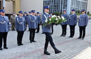 Policjant z wiązanką kwiatów podchodzi do pomnika. W tle umundurowani na galowo policjanci