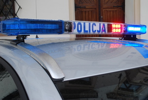 Na zdjęciu belka policyjnego radiowozu z napisem policja i z włączonymi światłami koloru  czerwonego.
