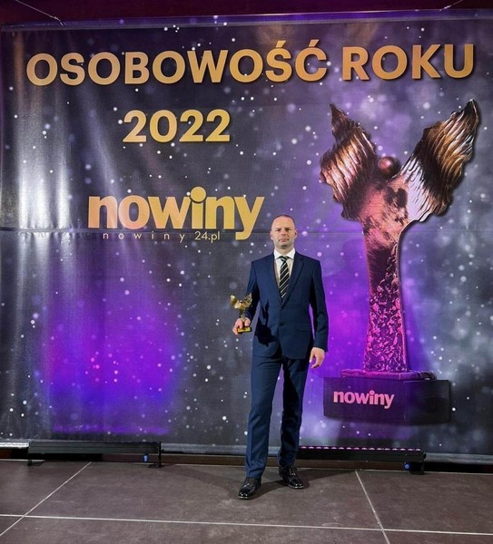 Policjant odznaczony statuetką w plebiscycie. W tle, nazwa konkursu Osobowość Roku 2022 Nowiny 24.pl