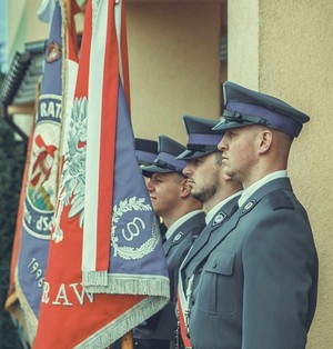 Policyjny poczet sztandarowy, funkcjonariusze w umundurowaniu wyjściowym w trakcie uroczystości rocznicowych przy budynku Starostwa Powiatowego w Krośnie