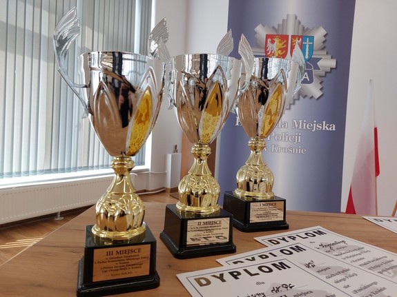 Puchary dla zwycięzców turnieju strzeleckiego oraz okolicznościowe dyplomy, w tle rolap z logotypem i napisem Komenda Miejska Policji w Krośnie