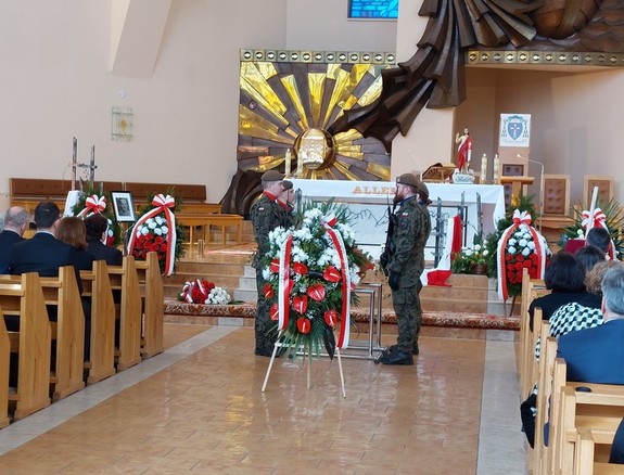 Wojskowa asysta honorowa przy trumnie podczas uroczystości pogrzebowych w kościele. Widoczne okolicznościowe wieńce oraz uczestnicy pogrzebu