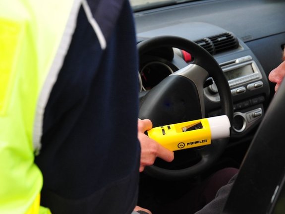 Na zdjęciu widoczny policjant ruchu drogowego przy pomocy urządzenia kontroluje u kierowców stan trzeźwości
