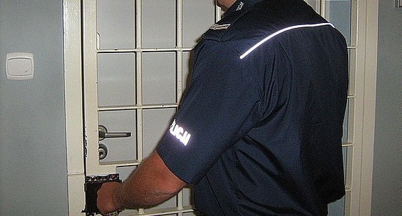 Umundurowany policjant zamykający drzwi do pomieszczenia dla osób zatrzymanych.