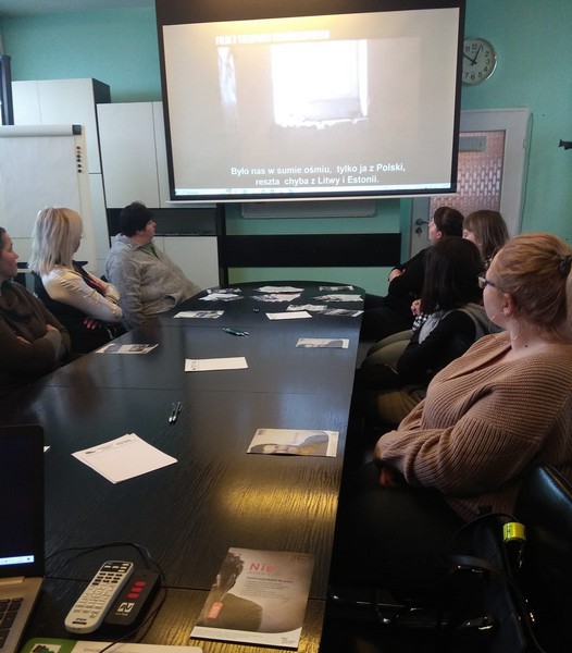 Uczestnicy spotkania w urzędzie pracy podczas prezentacji wyświetlanego filmu o tematyce handlu ludźmi. Na stolikach materiały informacyjne i piśmiennicze