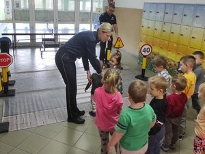Policjantka pokazująca dzieciom jak przechodzić przez przejście dla pieszych, które jest rozłożone na podłodze