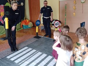 Policjanci pokazujący dzieciom znak zielonej sygnalizacji świetlnej przy przejściu dla pieszych