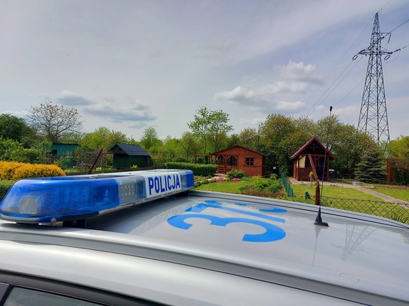 widok od strony dachu policyjnego radiowozu na którym jest policyjna belka z napisem policja na tle ogródków działkowych