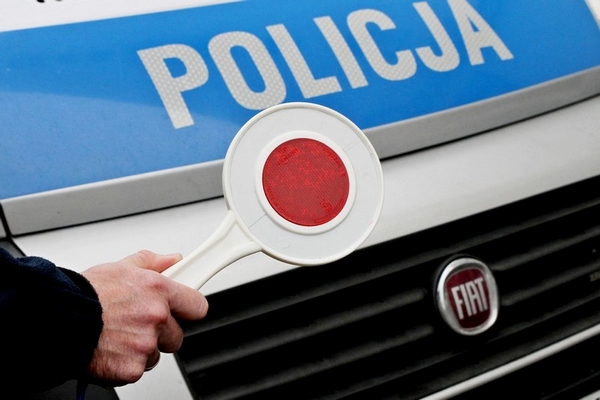 policjant trzymający w ręce tarczę do zatrzymywania pojazdów na tle radiowozu z napisem Policja
