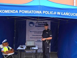 Policjant w namiocie z napisem Komenda Powiatowa Policji w Łańcucie rozdaje ulotki na temat mapy zagrożeń.