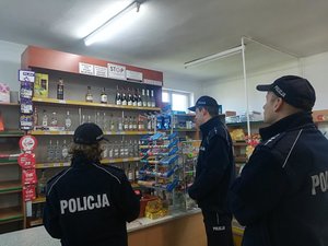 Troje policjantów stoi przy ladzie sklepu monopolowego. Sprawdzają dokumenty.