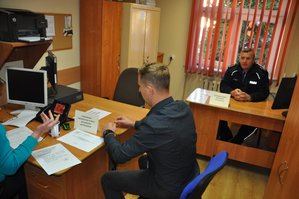 Rezerwista siedzi przy biurku. W tle policjant.