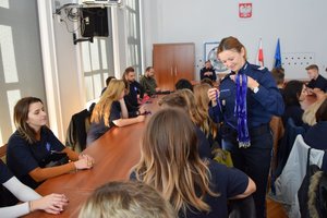 Policjanci podczas spotkania z uczniami w auli Komendy Wojewódzkiej Policji w Rzeszowie. Na pierwszym planie policjantka rozdaje niebieskie smycze.