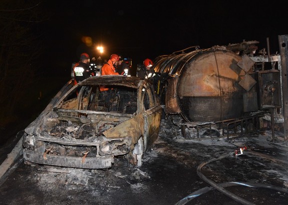 Spalone osobowe volvo oraz spalona cysterna, biorące udział w wypadku, w tle strażacy prowadzący akcję gaśniczą.