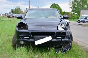 Uszkodzony przód w samochodzie marki Porsche Cayenne. W tle radiowóz policyjny.