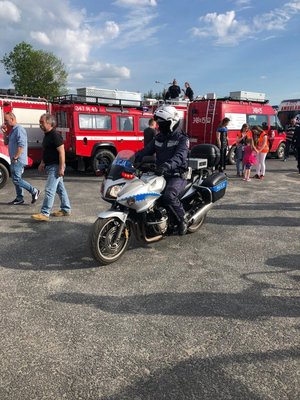 Policjant z Wydziału Ruchu Drogowego jadący na motocyklu, w tle wozy strażackie.
