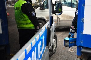 sylwetka policjanta trzymającego w ręku urządzenie do badania spalin na tle radiowozu