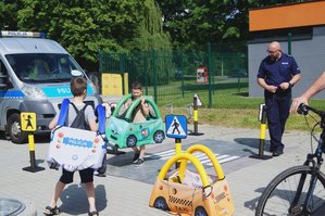 Policjant uczy przepisów wykorzystując autochodzik oraz makietę skrzyżowania.