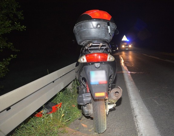 Uszkodzony motorower, który brał udział w zderzeniu z sarną, w tle radiowóz policyjny.