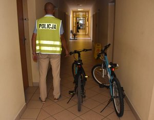 Zdjęcie kolorowe przedstawiające policjanta ubranego w kamizelkę odblaskową z napisem Policja. Po prawej stronie znajdują się dwa rowery.