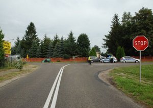 Fotografia przedstawia miejsce zdarzenia drogowego. Po prawej stronie znajdują się dwa radiowozy. Po lewej stronie widoczny jest uszkodzony samochód koloru zielonego.