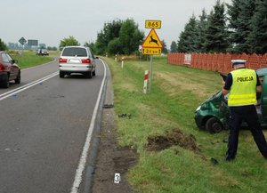 Zdjęcie przedstawia funkcjonariusza wykonującego czynności na miejscu zdarzenia drogowego.