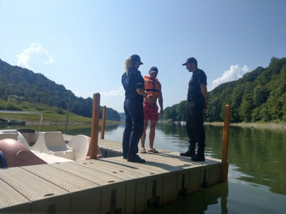 policjantka i strażak w trakcie rozmowy z turystą nad wodą