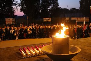 Zdjęcie przedstawia plac przed pomnikiem Walk i Męczeństwa w Jarosławiu. Widać na nim palący się znicz oraz w tle osoby  które biorą udział w uroczystościach.