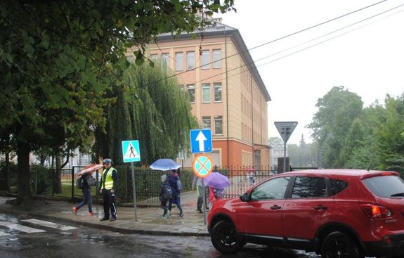 Zdjęcie przedstawia przejście dla pieszych w okolicy szkoły. Przed przejściem policjant.