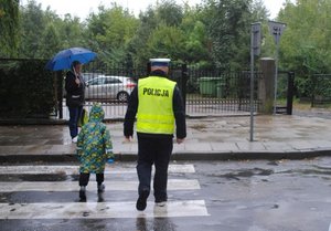 Na fotografii widoczny jest policjant, który przeprowadza dziecko przez przejście dla pieszych.