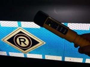 Zdjęcie przedstawia urządzenie do badania stanu trzeźwości na tle odblasku z logo ruchu drogowego
