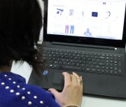 Na zdjęciu siedząca tyłem kobieta, która  korzysta z komputera.