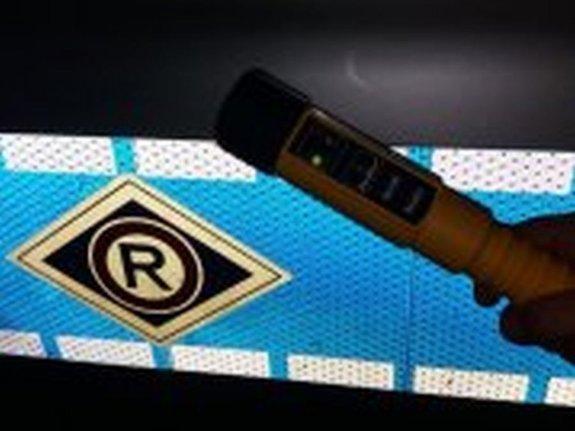 Zdjęcie przedstawia urządzenie do pomiaru zawartości alkoholu w wydychanym powietrzu  na tle radiowozu.
