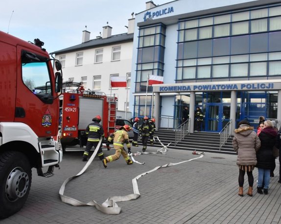 Plac przed budynkiem KPP Jarosław. Widoczny jest wóz bojowy PSP, osoby ewakuowane z budynku KPP, strażacy w czasie akcji.