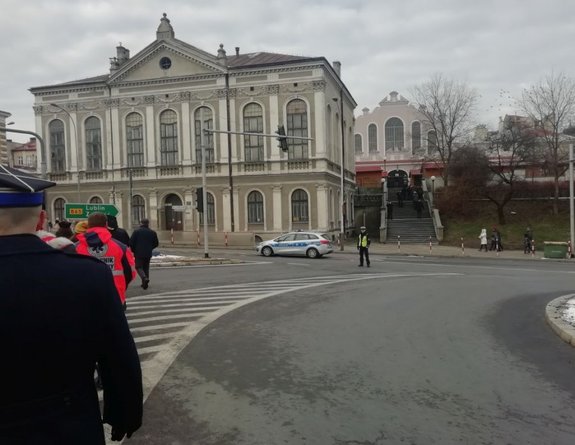 Radiowóz przy którym stoi policjant. Funkcjonariusz zabezpiecza przemarsz ludności.