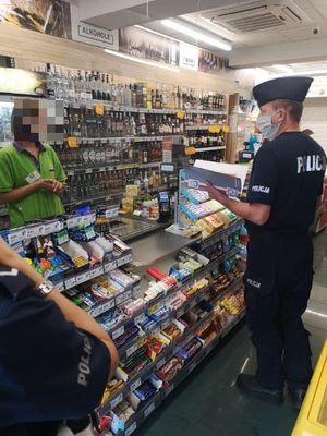 Policjant rozmawiający z ekspedientką podczas kontroli sklepu dokonywanej pod kątem sprzedaży alkoholu osobom nieletnim.