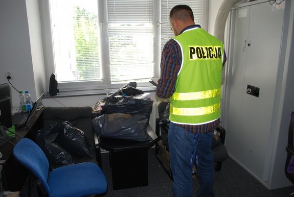 Na zdjęciu policjant z wydziału do walki z przestępczością gospodarcza i zabezpieczona podrobiona odzież.