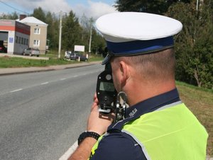 policjant ruchu drogowego stojący przy drodze wykonuje pomiar laserowym miernikiem prędkości