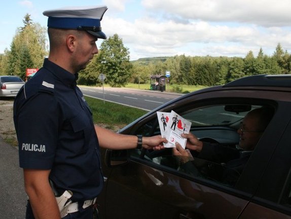 policjant wydziału ruchu drogowego wręcza kierowcy pakiet ulotek profilaktycznych