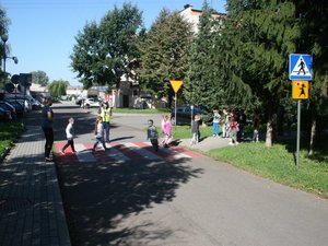 policjant ruchu drogowego przeprowadza przez przejście dla pieszych grupę dzieci