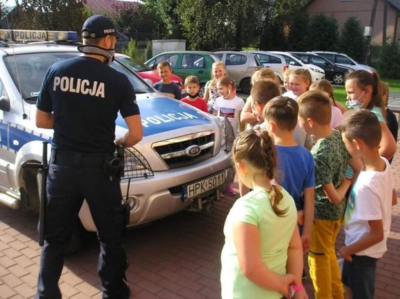Policjant z grupką dzieci stoi przy radiowozie.