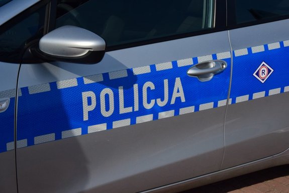 na zdjęciu element karoserii policyjnego radiowozu w kolorze srebrnym i napis policja na niebieskim tle